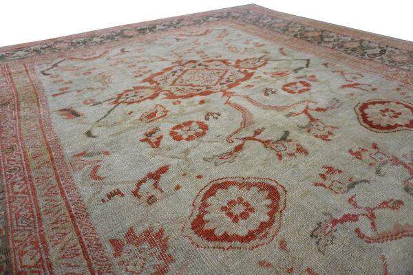 Close-up view of a textured rug corner showing a beige field, rust patterns, and multicolored decorative borders.