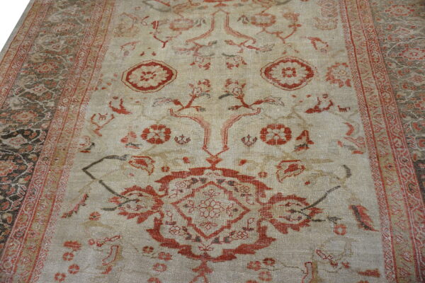 Close-up of a low pile rug featuring a light beige field, distressed rust patterns, and a dark ornate border.
