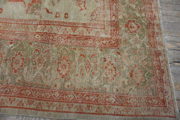 Distressed traditional rug in tan, olive, and rust hues showing low pile over wooden planks.