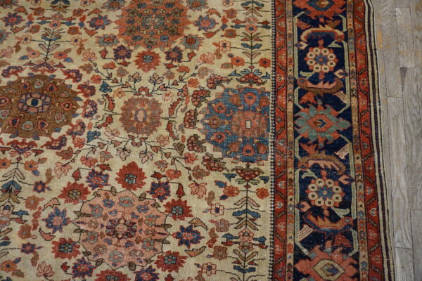Beige rug with intricate red and blue floral medallions and a navy border on light wood flooring.