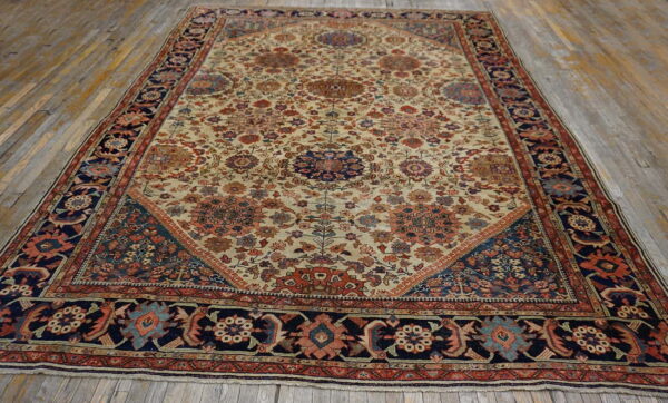 Cream rug with intricate floral designs, navy blue border, and terracotta accents on distressed wood floor.