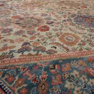 Low-pile rug showing intricate floral patterns in light beige, blue, and coral tones with a teal border.
