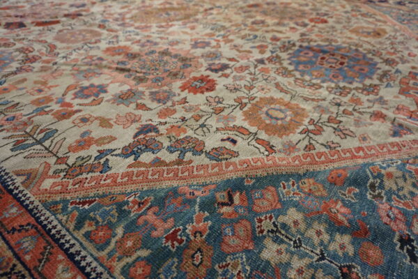 Low-pile rug showing intricate floral patterns in light beige, blue, and coral tones with a teal border.
