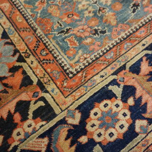Ornate rug corner featuring floral motifs and nested borders in navy, teal, orange, and cream colors.