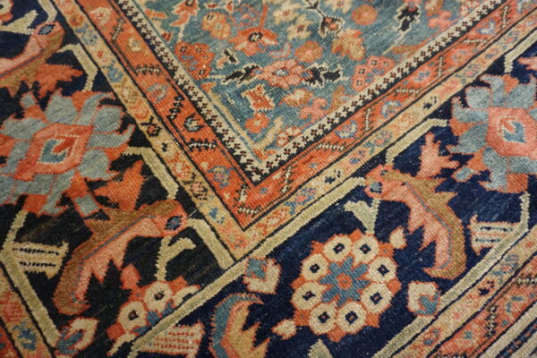Ornate rug corner featuring floral motifs and nested borders in navy, teal, orange, and cream colors.