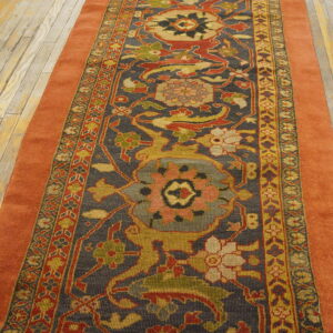 A runner featuring a detailed dark blue, red, and gold floral pattern, bordered by solid rust orange, on wood floors.