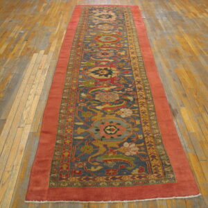 Rust and blue floral runner rug with complex patterns displayed on worn hardwood flooring.