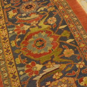 Rust orange bordered rug with a complex floral pattern in olive, red, and gold on a dark blue field.