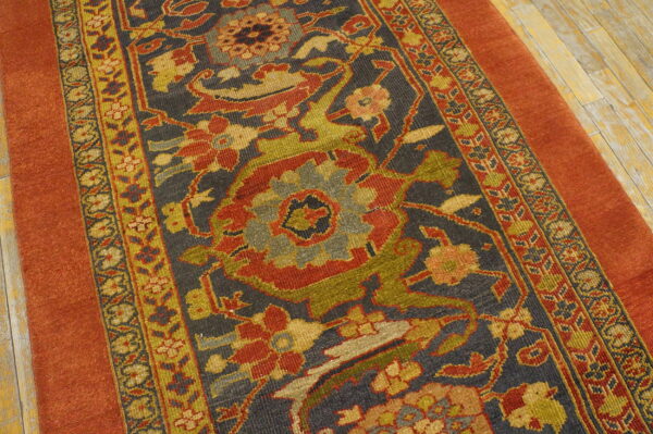 Rust orange bordered rug with a complex floral pattern in olive, red, and gold on a dark blue field.