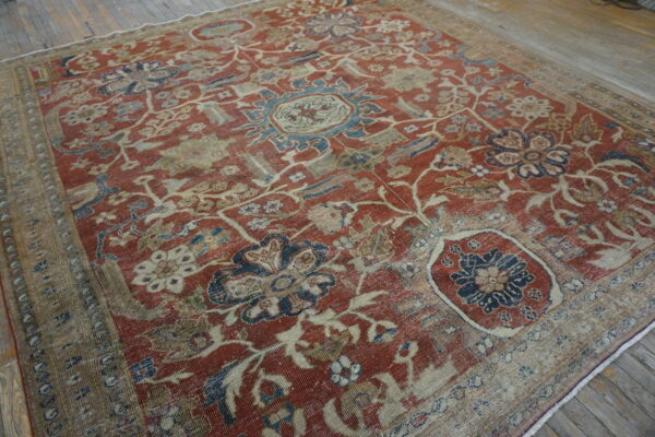 Low-pile floral rug featuring red, navy, and beige colors displays heavy wear on rustic wood planks.