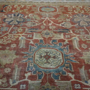 Low-pile rug with worn texture, displaying an intricate red, blue, and beige traditional medallion pattern.