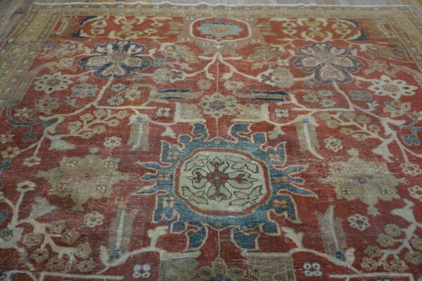 Low-pile rug with worn texture, displaying an intricate red, blue, and beige traditional medallion pattern.