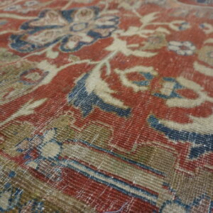 Distressed rug close-up featuring traditional red, indigo, and beige floral designs with minimal pile.
