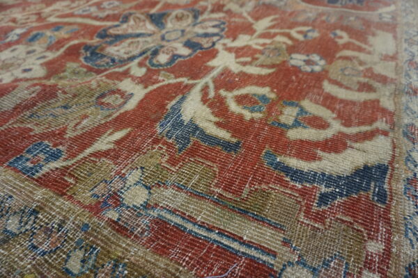 Distressed rug close-up featuring traditional red, indigo, and beige floral designs with minimal pile.