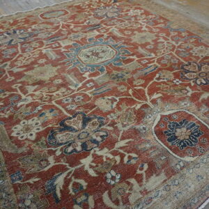 Faded red and beige rug featuring a large distressed floral pattern on rustic wood flooring.