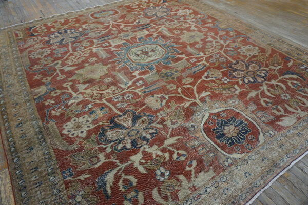 Faded red and beige rug featuring a large distressed floral pattern on rustic wood flooring.