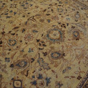 Low-pile golden rug displaying faded ornate floral and vine patterns in brown, blue, and rust colors.