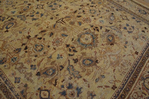 Low-pile golden rug displaying faded ornate floral and vine patterns in brown, blue, and rust colors.