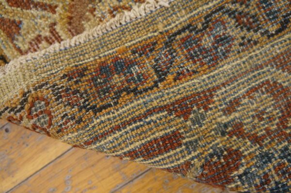 A tightly woven rug with rust, blue, and gold patterns is folded over distressed light wood flooring.