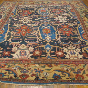 Low-pile rug features navy, rust, blue, and tan traditional patterns on a brown hardwood floor.