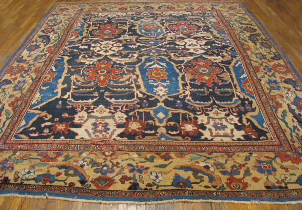 Low-pile rug features navy, rust, blue, and tan traditional patterns on a brown hardwood floor.