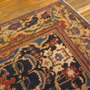 Navy and tan patterned rug with red and blue floral motifs rests on golden hardwood planks.