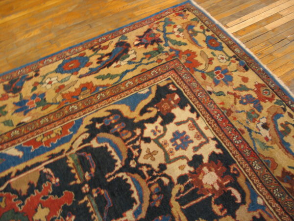 Navy and tan patterned rug with red and blue floral motifs rests on golden hardwood planks.