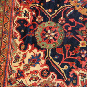 Intricate navy, red, cream, and green floral patterns cover the dense pile of this traditional rug.