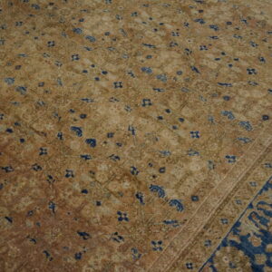 Distressed tan rug with scattered blue medallions and a wide ornate border featuring bold indigo and beige patterns.