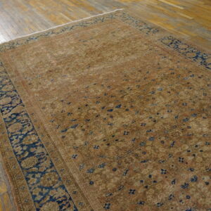Traditional low-pile rug with a detailed tan and copper field bordered by deep navy blue on distressed wood planks.