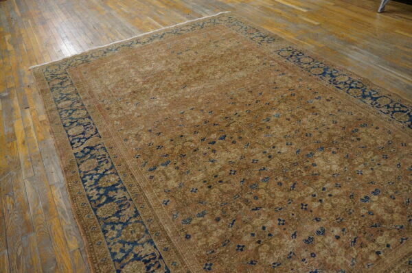 Traditional low-pile rug with a detailed tan and copper field bordered by deep navy blue on distressed wood planks.