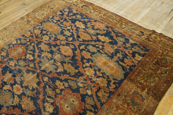 Low-pile rug with dense blue and gold floral patterns rests diagonally on light-toned hardwood flooring.