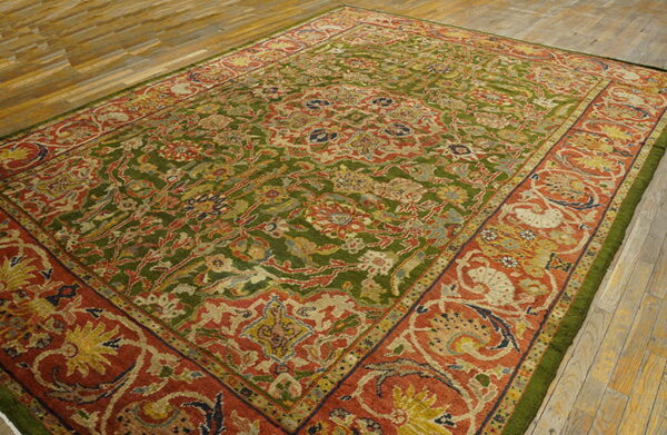 Ornate rug with an olive green field and a wide rust red floral border on wood floors.