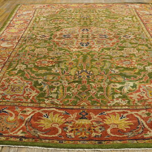Large rug featuring a dense floral pattern with olive green field and wide rust borders on a wood floor.