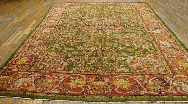 Large rug featuring a dense floral pattern with olive green field and wide rust borders on a wood floor.