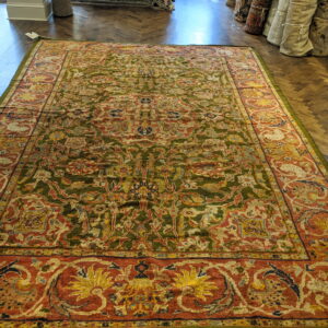 Ornate traditional rug with an olive green field and rust border rests on dark herringbone wood flooring.