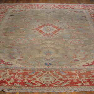 A large traditional rug with a muted gray field and red-orange floral border sits on wood flooring.