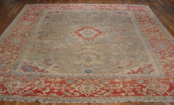 A large traditional rug with a muted gray field and red-orange floral border sits on wood flooring.
