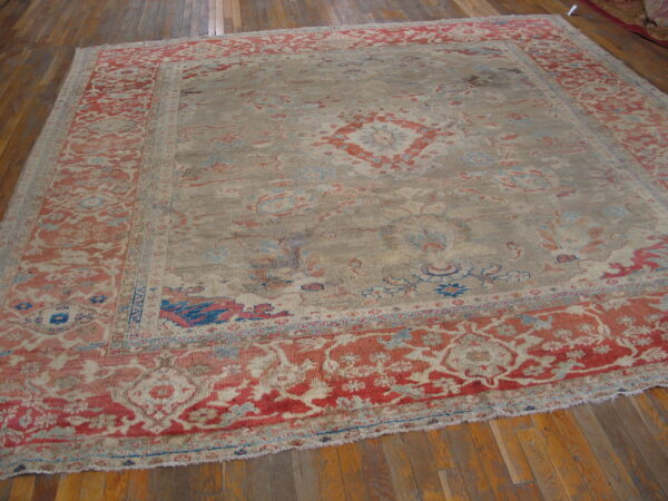 Faded traditional area rug with a beige field, coral red borders, and blue accents on wood plank flooring.