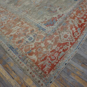 Traditional patterned rug with coral, blue, and beige details, shown on distressed gray and yellow hardwood flooring.