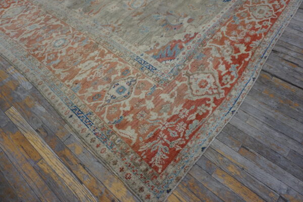 Traditional patterned rug with coral, blue, and beige details, shown on distressed gray and yellow hardwood flooring.