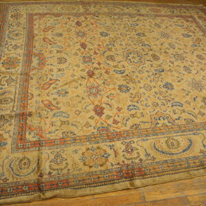 Traditional square rug in beige, blue, and orange floral patterns rests on wood plank flooring.