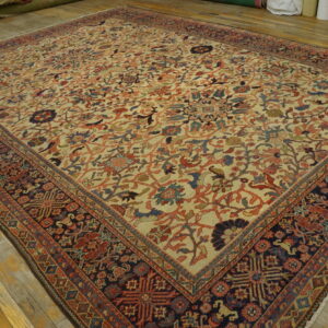 Low-pile floral rug with a cream field and navy blue border, displayed on distressed yellow wood flooring.