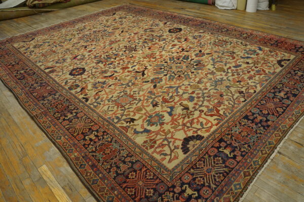 Low-pile floral rug with a cream field and navy blue border, displayed on distressed yellow wood flooring.