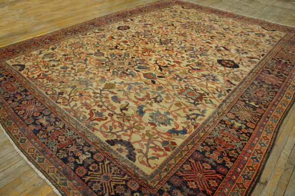 Large traditional rug featuring a light floral field and dark, patterned borders on worn wood flooring.