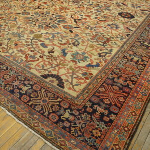 Cream rug with dense floral patterns and a dark blue geometric border lies on yellow-toned hardwood flooring.