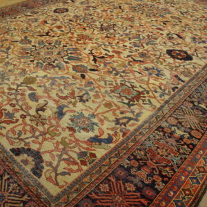 Low-pile rug with muted red and blue floral motifs on a tan ground over worn wood flooring.