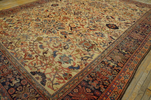 Low-pile rug with muted red and blue floral motifs on a tan ground over worn wood flooring.