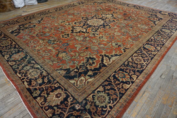 Square rug featuring a dense floral pattern in rust, navy, and gold on distressed gray wood flooring.