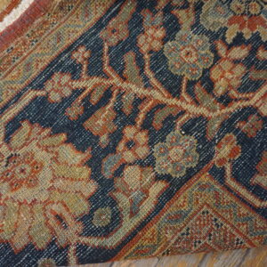Close-up of a low pile rug displaying a dense traditional pattern in navy, rust, gold, and green tones.